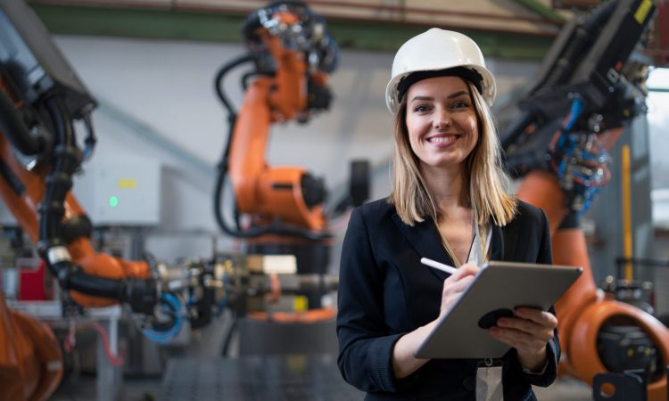 A female chief engineer in modern industrial factory using tablet and making audit. Long angle view.