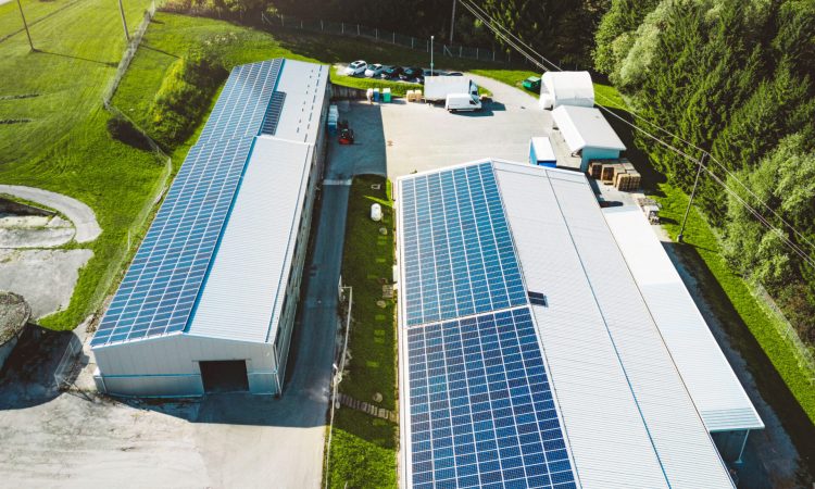 Solar panels installed on a roof of a large industrial building or a warehouse. Industrial building in the country side of Slovenia with residential houses in the background. High quality photo